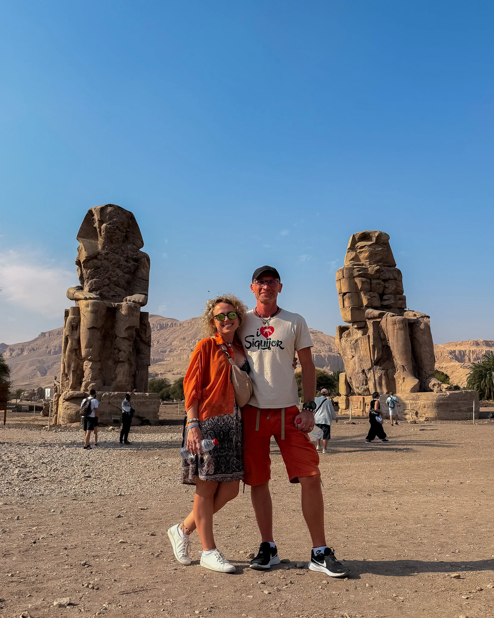 Agata i Paweł stoją przed Kolosami Memnona w Luksorze; w tle monumentalne kamienne posągi i pustynny krajobraz.