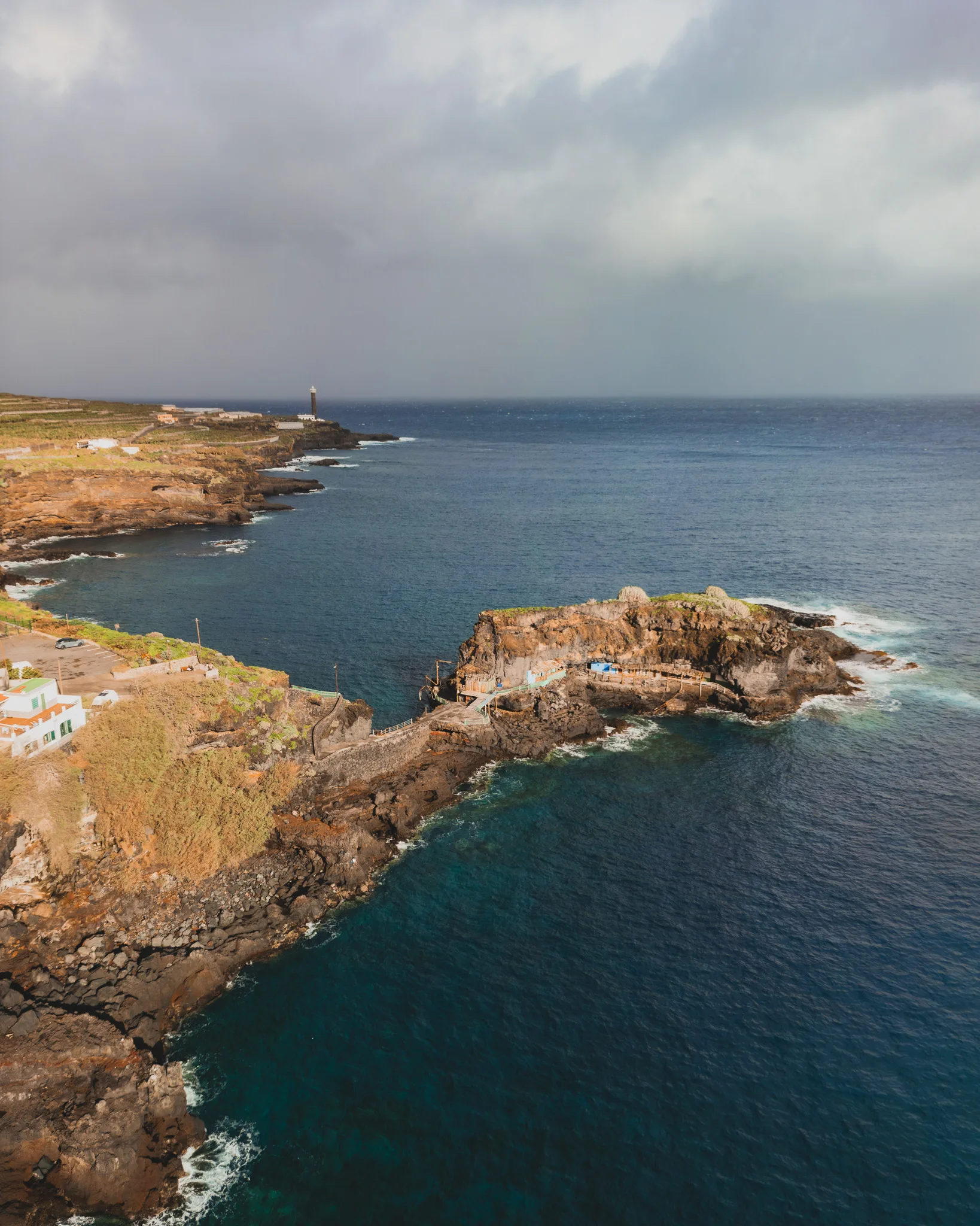 Widok z drona na skaliste wybrzeże i ocean z małą zatoką oraz latarnią morską w oddali - Puerto de Talavera - La Palma