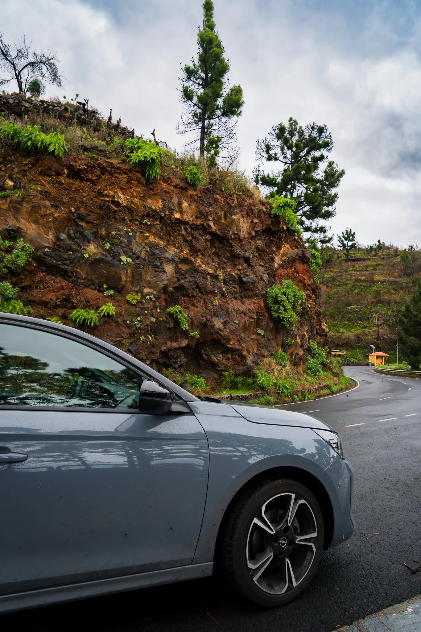Samochód na krętej górskiej drodze na La Palmie, wulkaniczne skały i zielona roślinność.