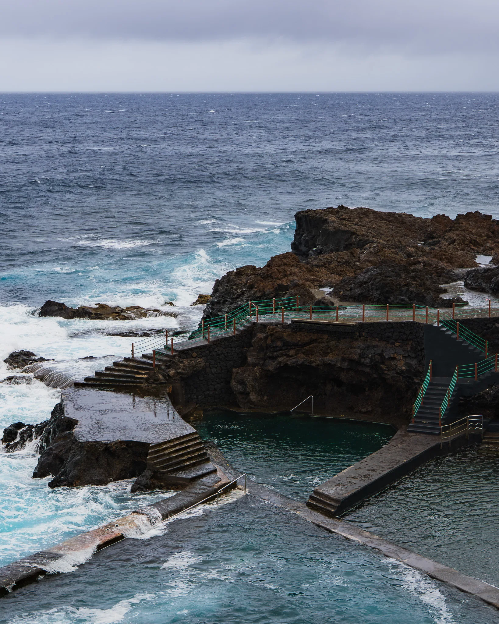 Skaliste wybrzeże La Palmy z turkusowym oceanem i falami rozbijającymi się o klify, pochmurny dzień