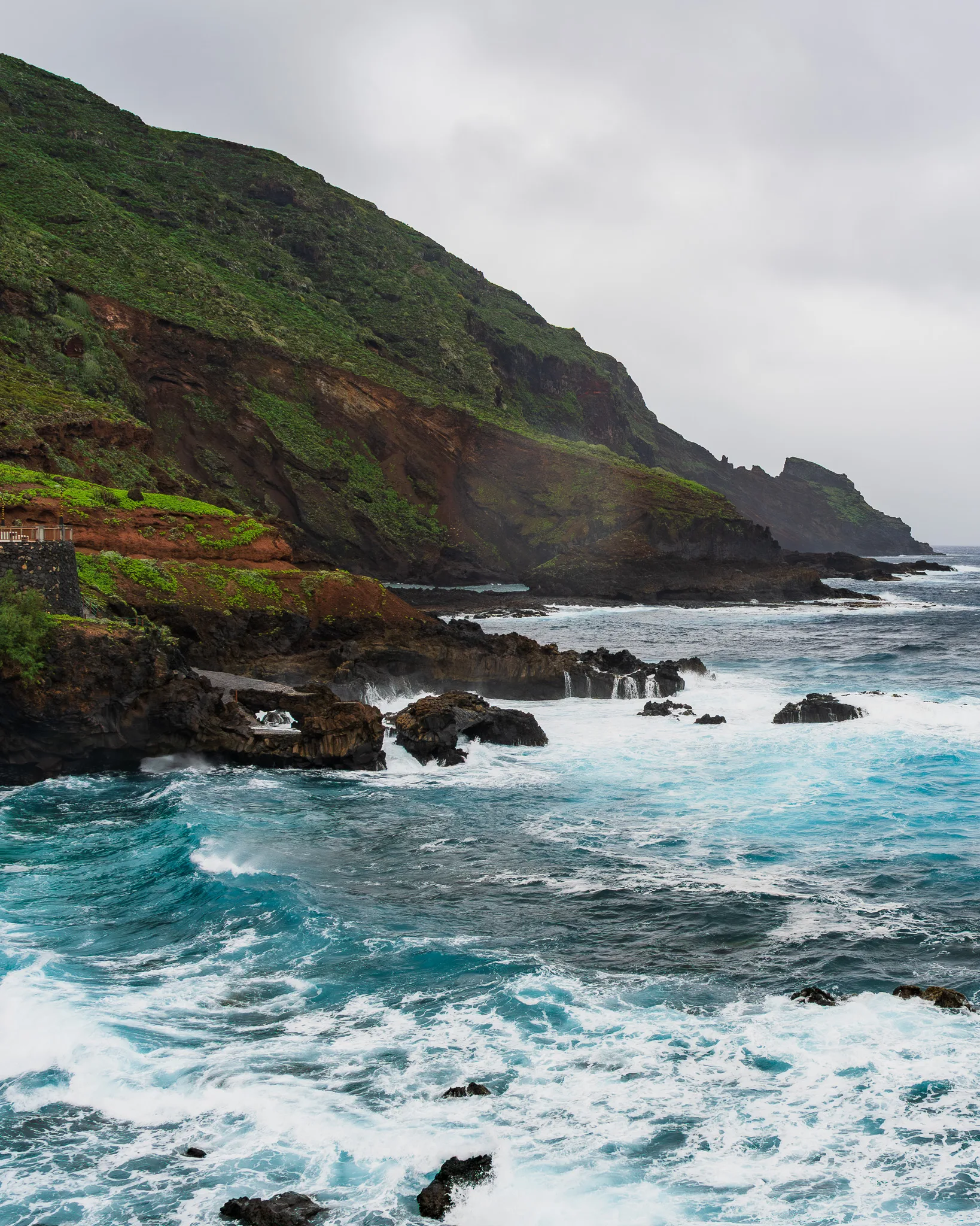 Skaliste wybrzeże La Palmy z turkusowym oceanem i falami rozbijającymi się o klify, pochmurny dzień