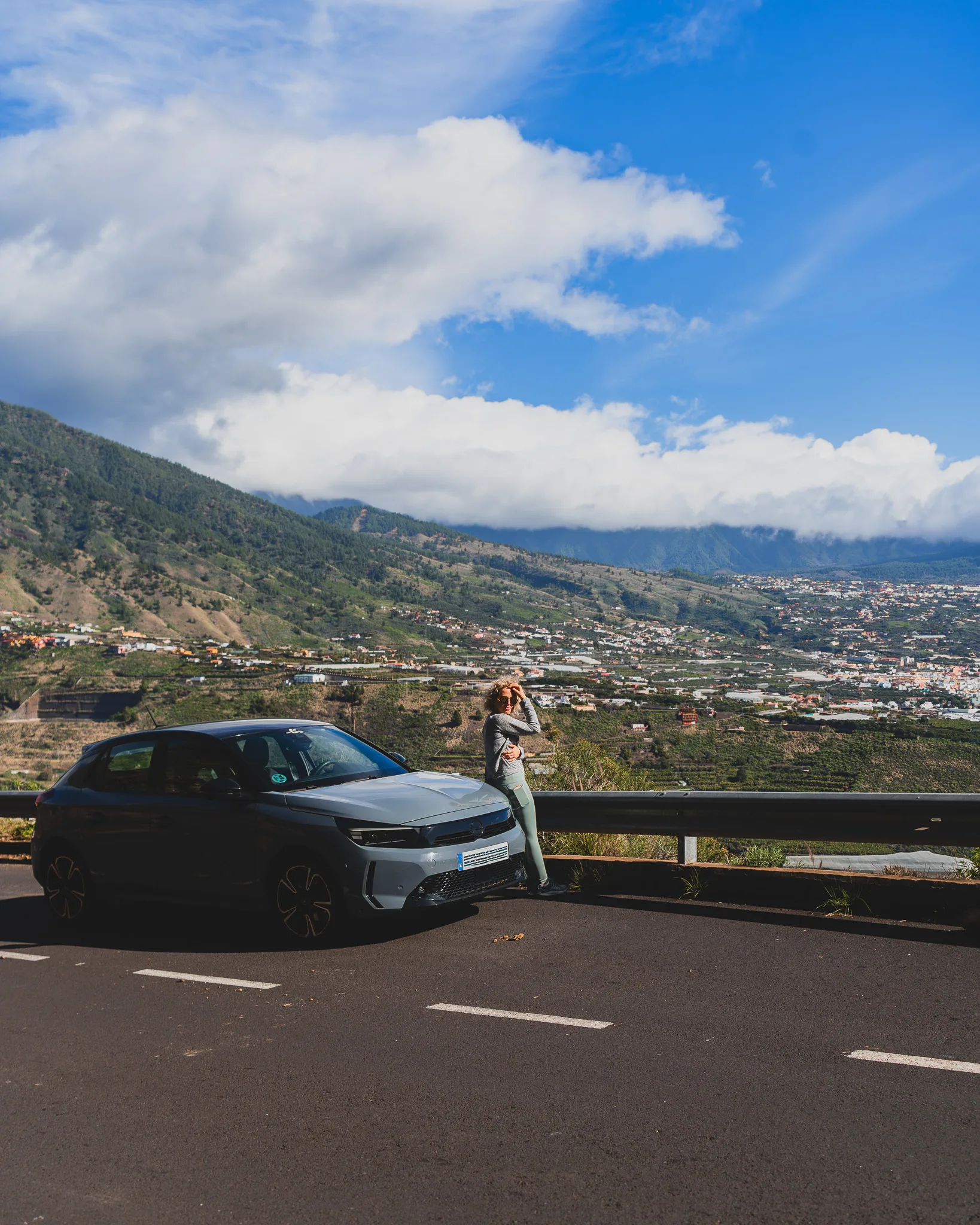 Samochód zaparkowany przy górskiej drodze na La Palmie, panorama doliny i zabudowy poniżej.