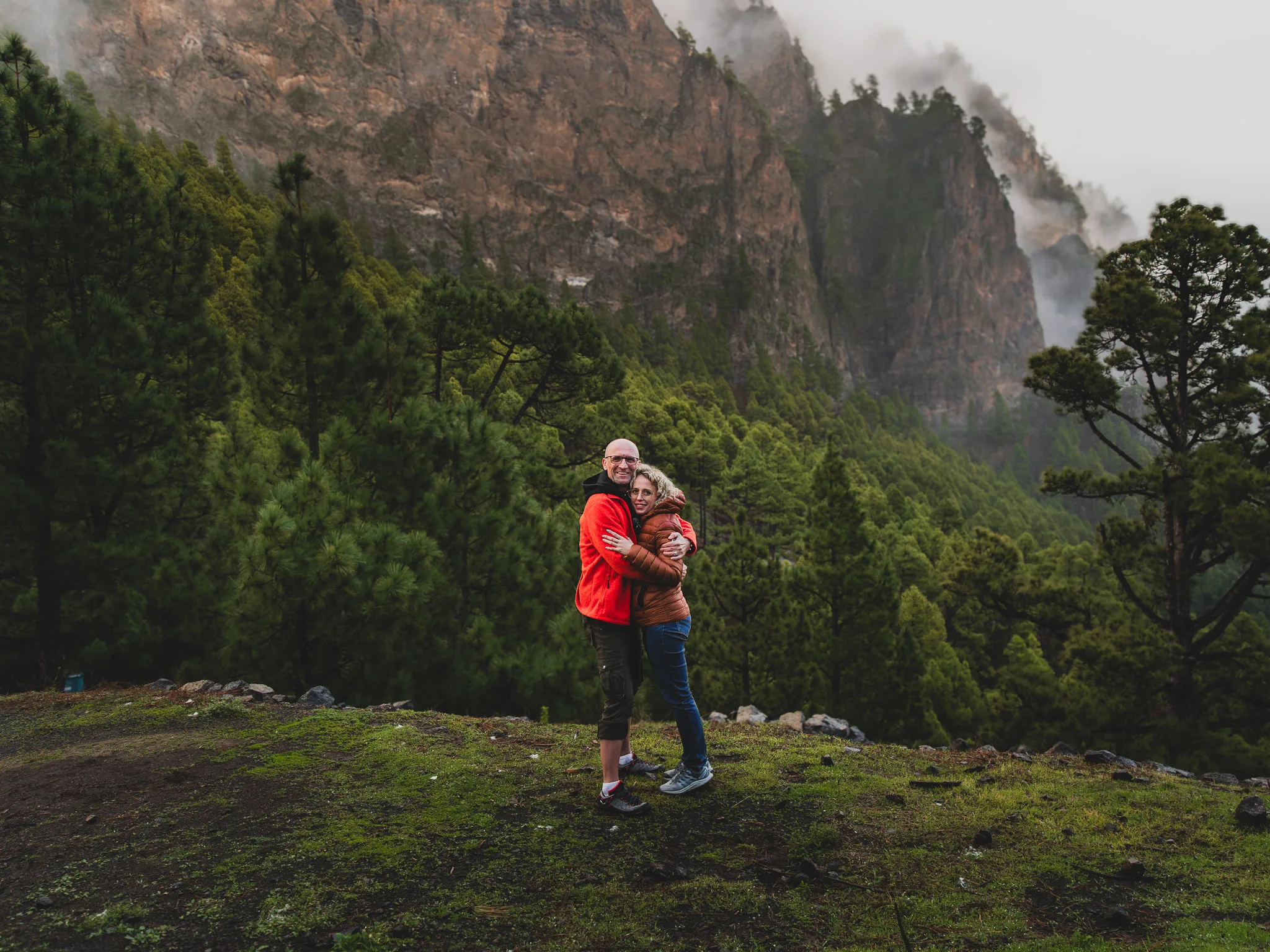 Para obejmująca się na tle zielonego lasu i stromych gór spowitych chmurami, surowy krajobraz La Palmy.
