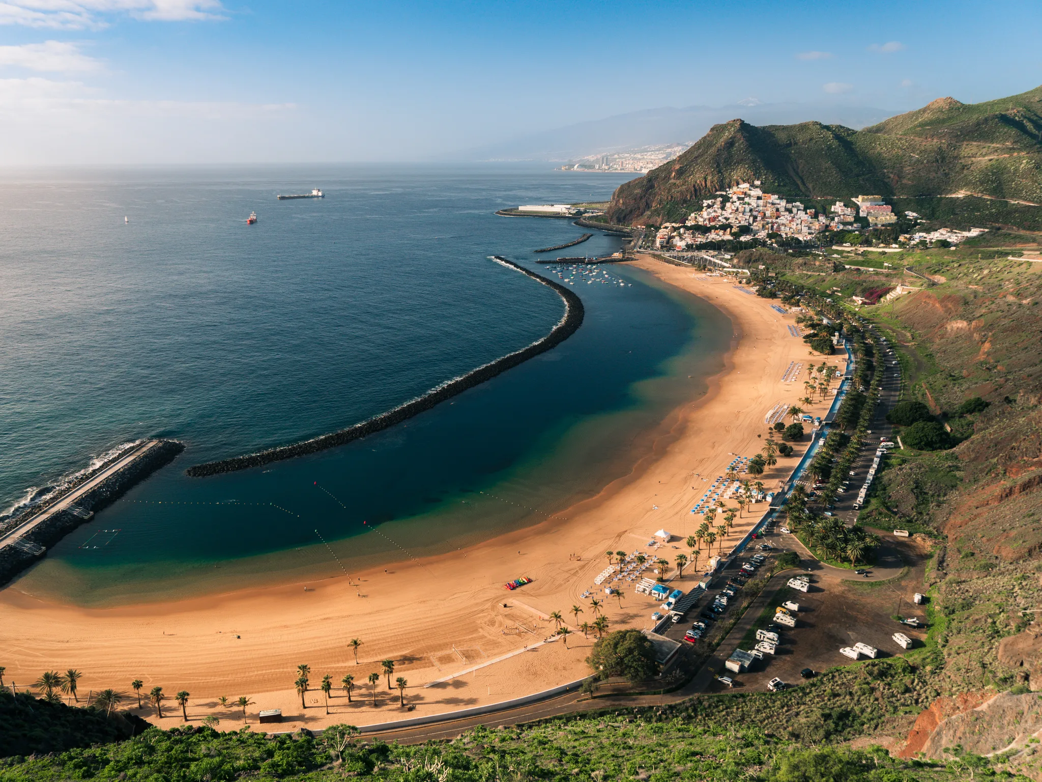 Panoramiczny widok na Playa de Las Teresitas – szeroka, piaszczysta plaża z charakterystycznymi falochronami, turkusową wodą Atlantyku i miasteczkiem San Andrés u stóp zielonych wzgórz Teneryfy.