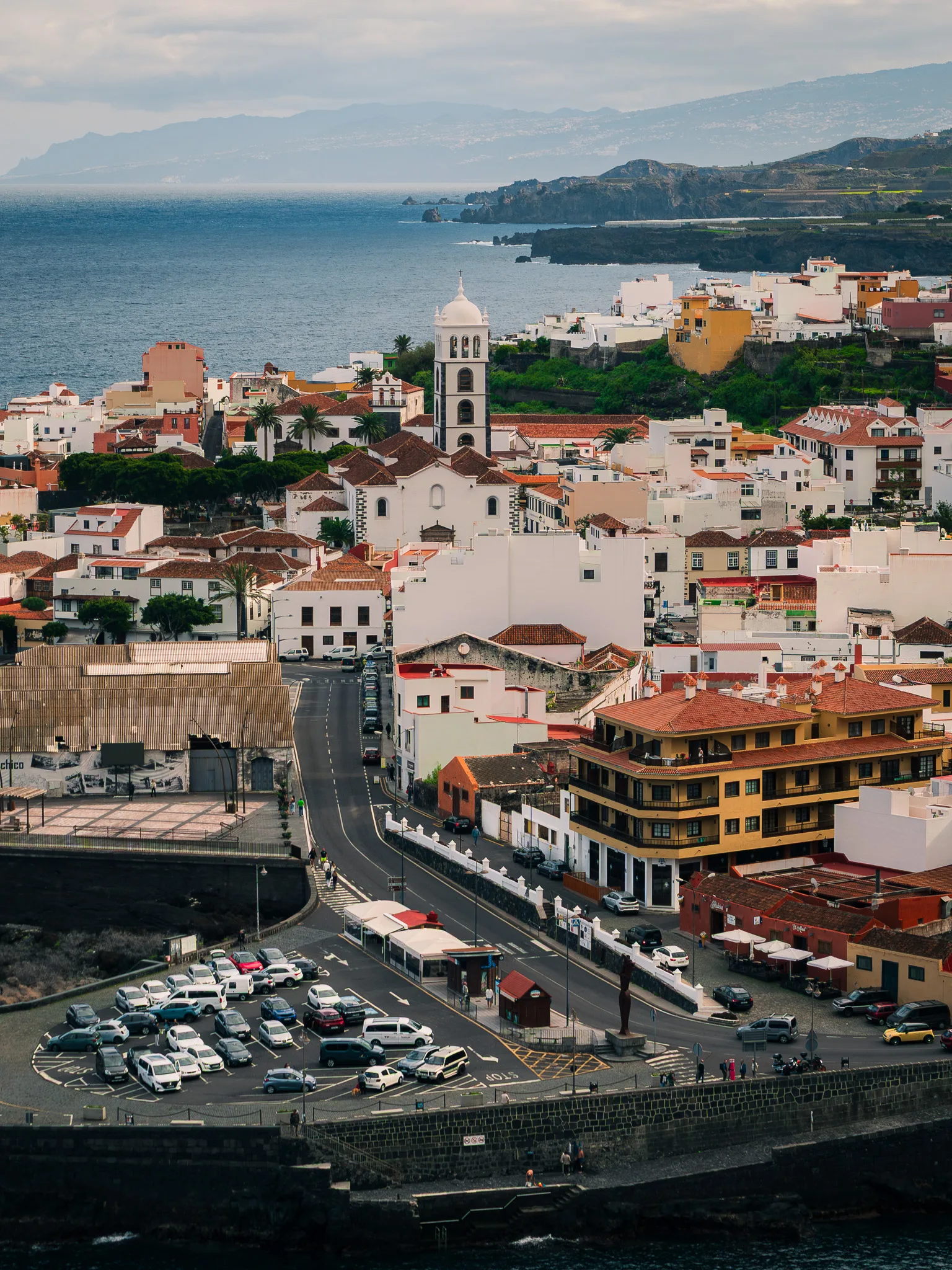 Panorama Garachico od strony oceanu – zabudowa miasteczka rozciągnięta wzdłuż wybrzeża, charakterystyczna wieża kościoła i skaliste klify Teneryfy w oddali.