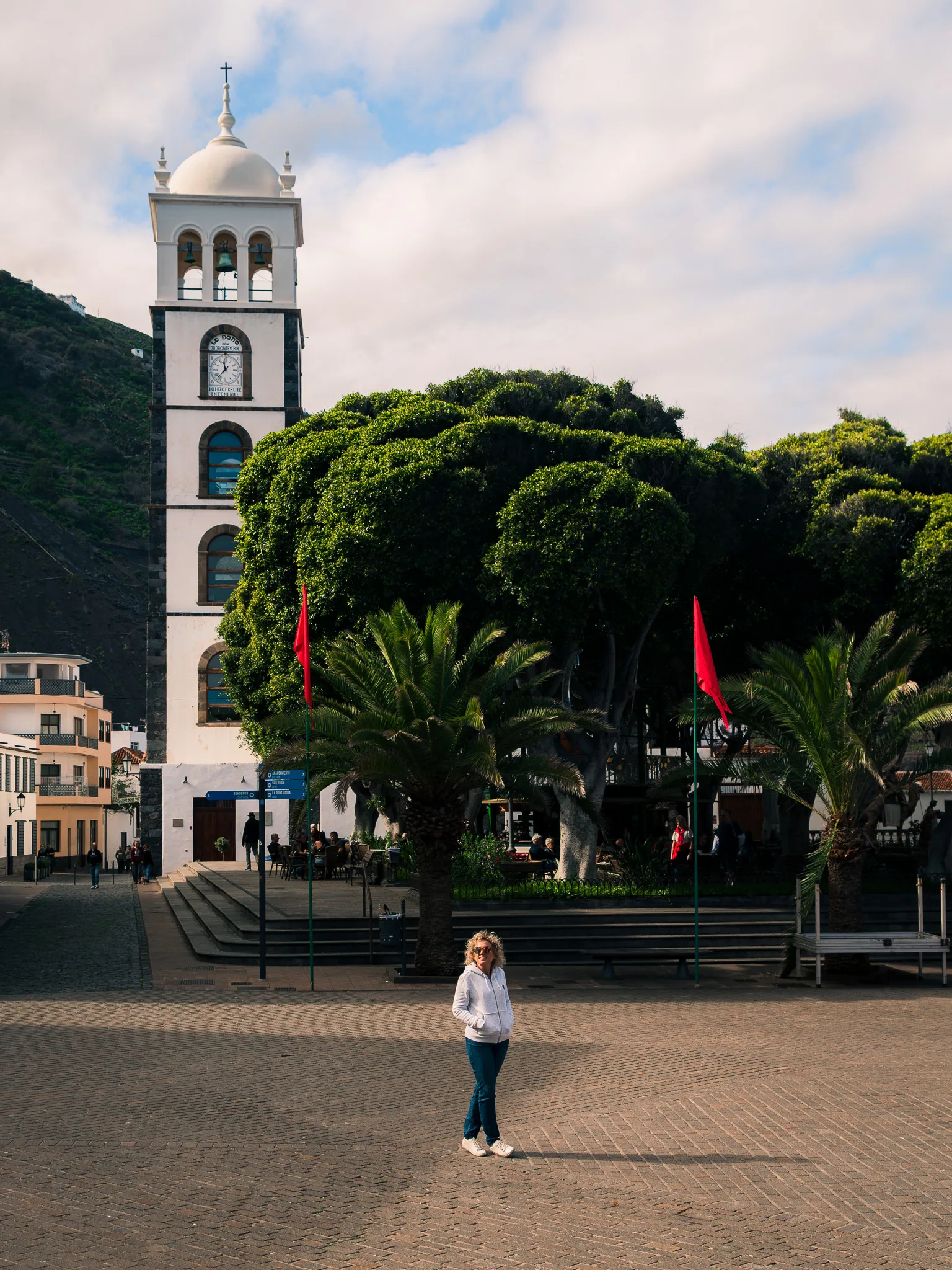 Plac w miasteczku Garachico – sylwetka osoby na tle białej wieży kościoła, palmy i zielone drzewa, spokojna atmosfera historycznego centrum.