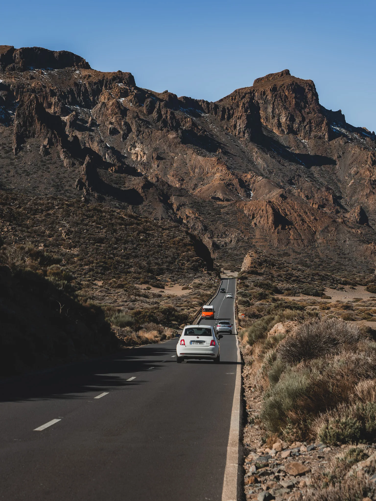 Droga przez Park Narodowy Teide – asfaltowa szosa przecinająca pustynny, wulkaniczny krajobraz, samochody jadące w kierunku skalistych formacji górskich pod bezchmurnym niebem.