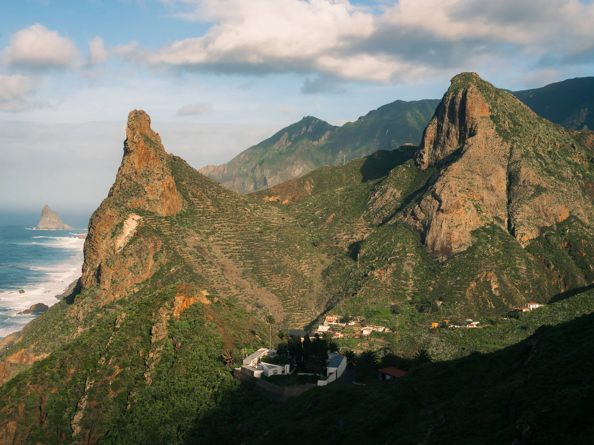 Panorama gór Anaga na Teneryfie – strome, zielone zbocza i skalne iglice opadające w stronę oceanu, rozproszone domy w dolinie.