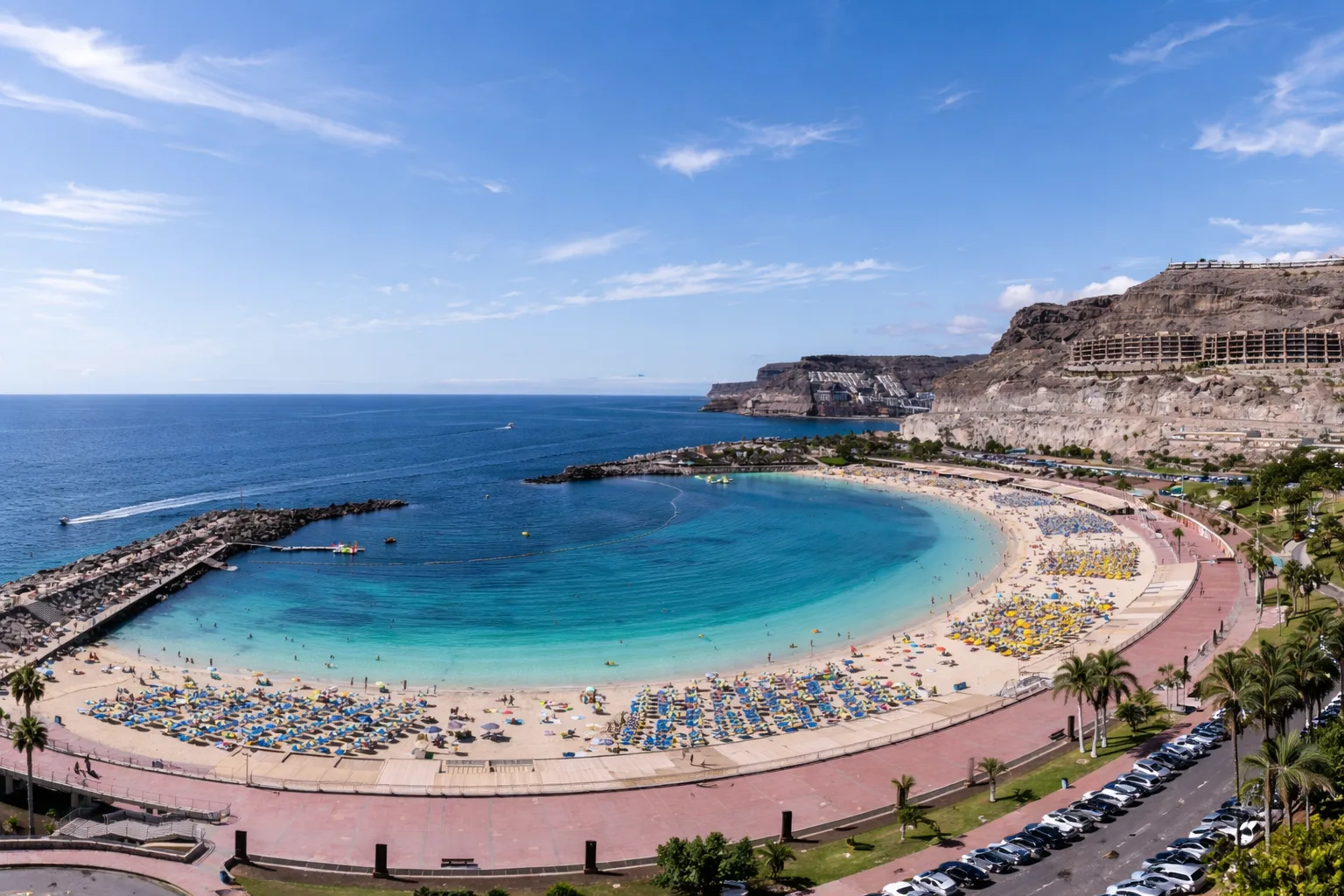 Plaża Amadores na Gran Canarii z lotu ptaka, turkusowa zatoka w kształcie półksiężyca, złoty piasek, leżaki i klify z hotelami w tle, słoneczny dzień