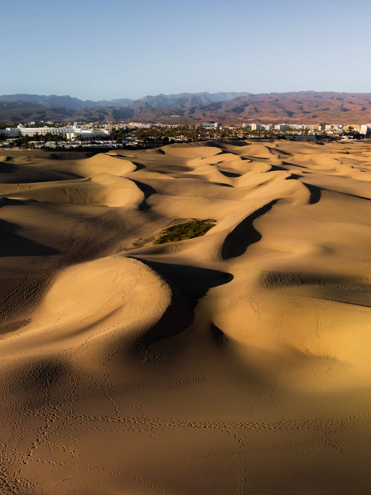 Gran Canaria: wydmy Maspalomas z lotu drona, piaszczyste fale i ślady na piasku, w tle miasto i góry