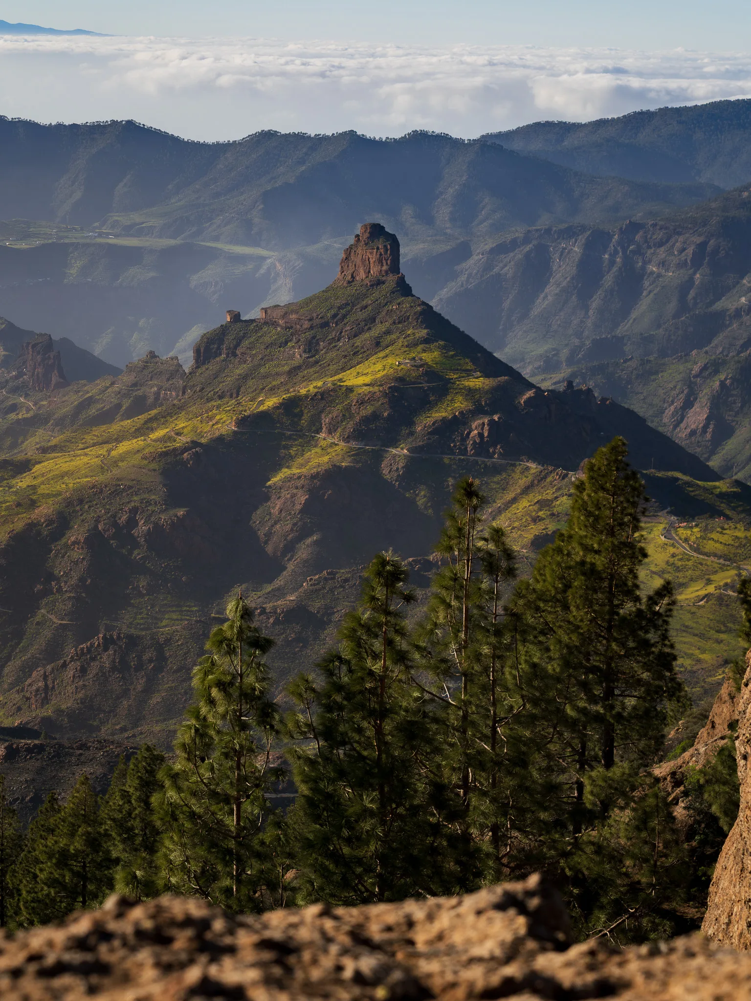 Gran Canaria: widok na zielone zbocza i charakterystyczną skalną formację na szczycie, ponad chmurami w tle. Wyspy Kanaryjskie