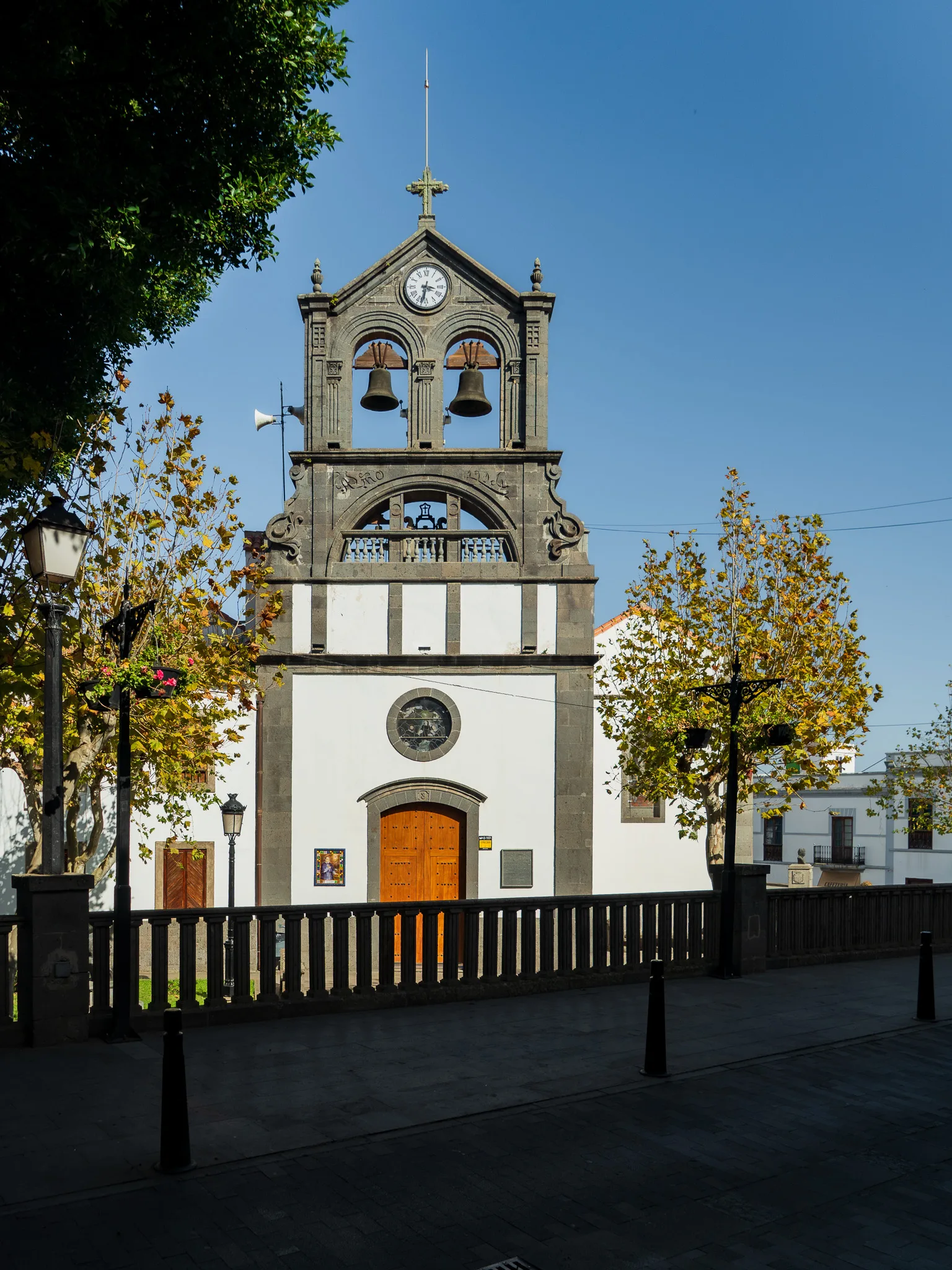 Gran Canaria: Firgas – kościół z wieżą zegarową i dzwonami na tle błękitnego nieba, plac miasteczka