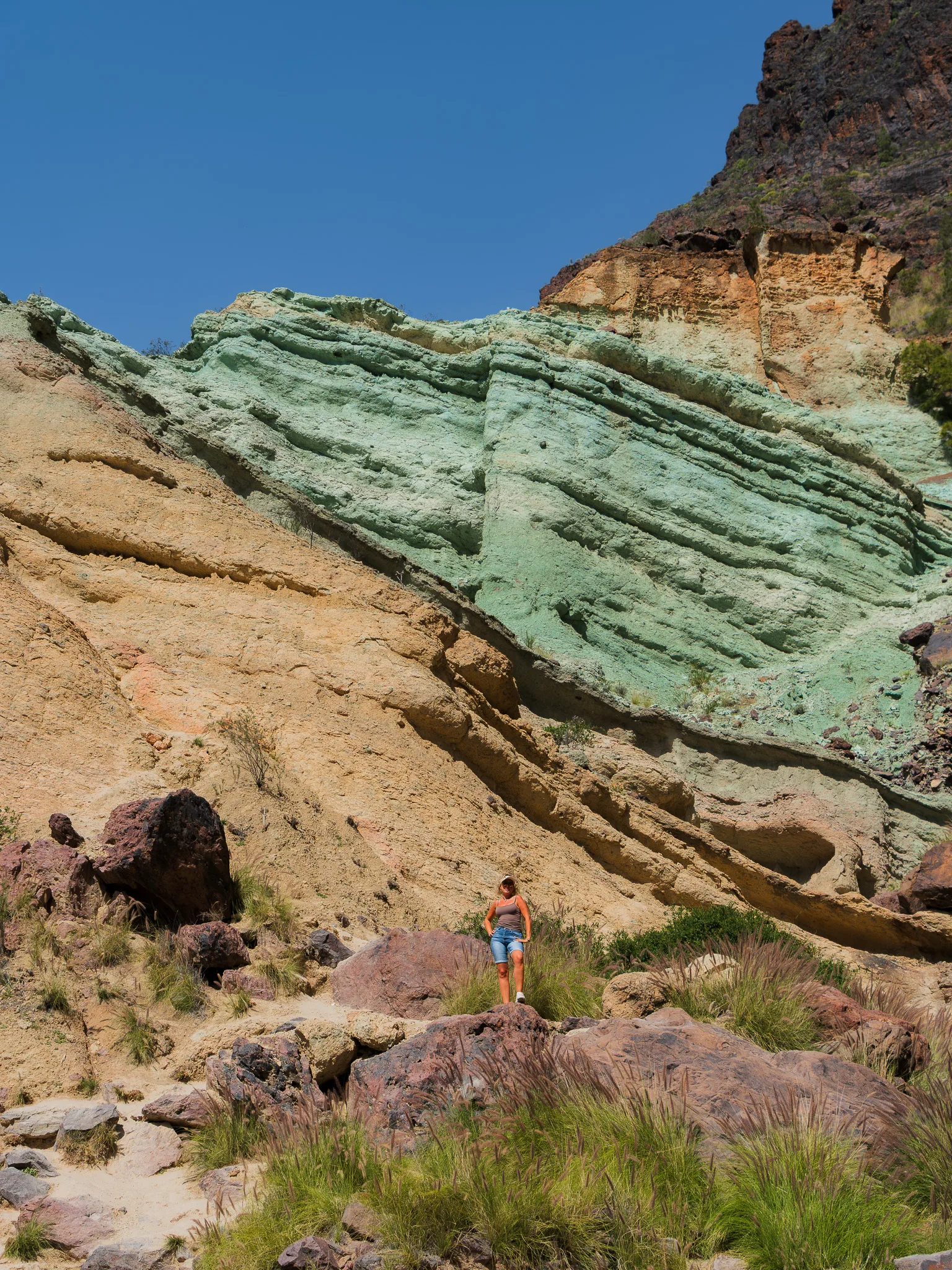 Gran Canaria: kolorowe warstwy skał w wąwozie, kobieta na szlaku wśród wulkanicznych głazów