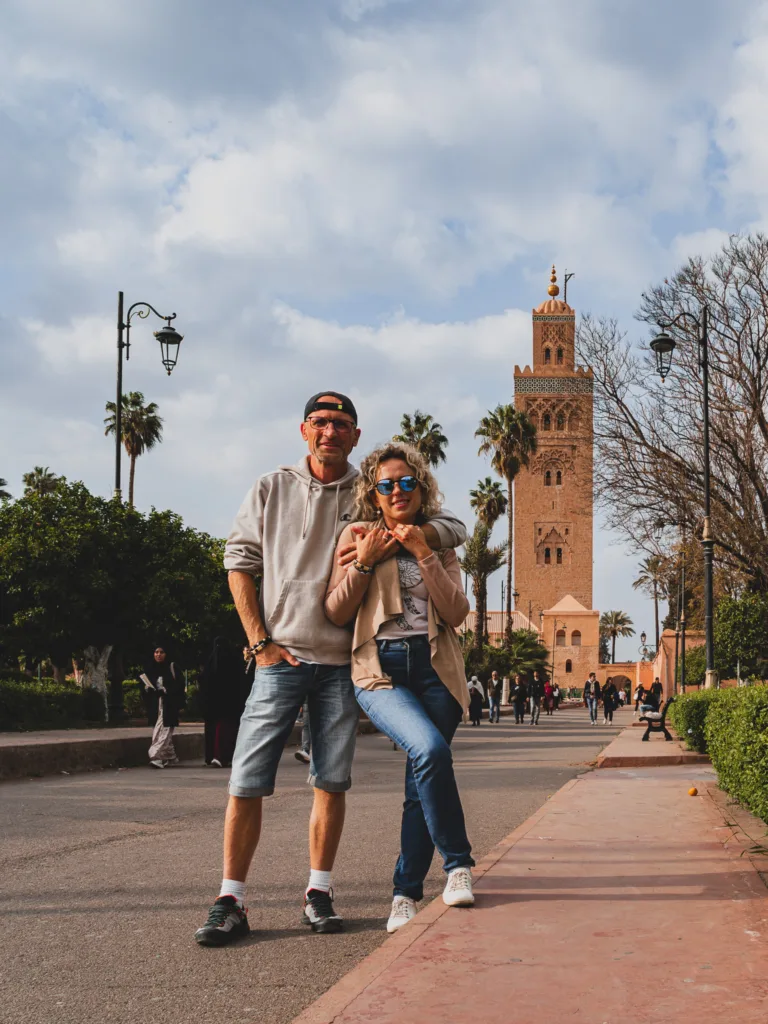 Marrakesz: para turystów pozuje na alejce w centrum miasta, a w tle widać minaret meczetu Kutubijja i palmy.