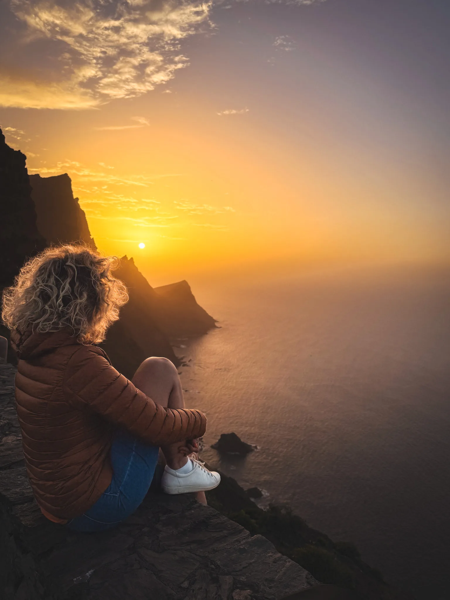Gran Canaria: kobieta siedzi na krawędzi klifu i ogląda zachód słońca nad oceanem