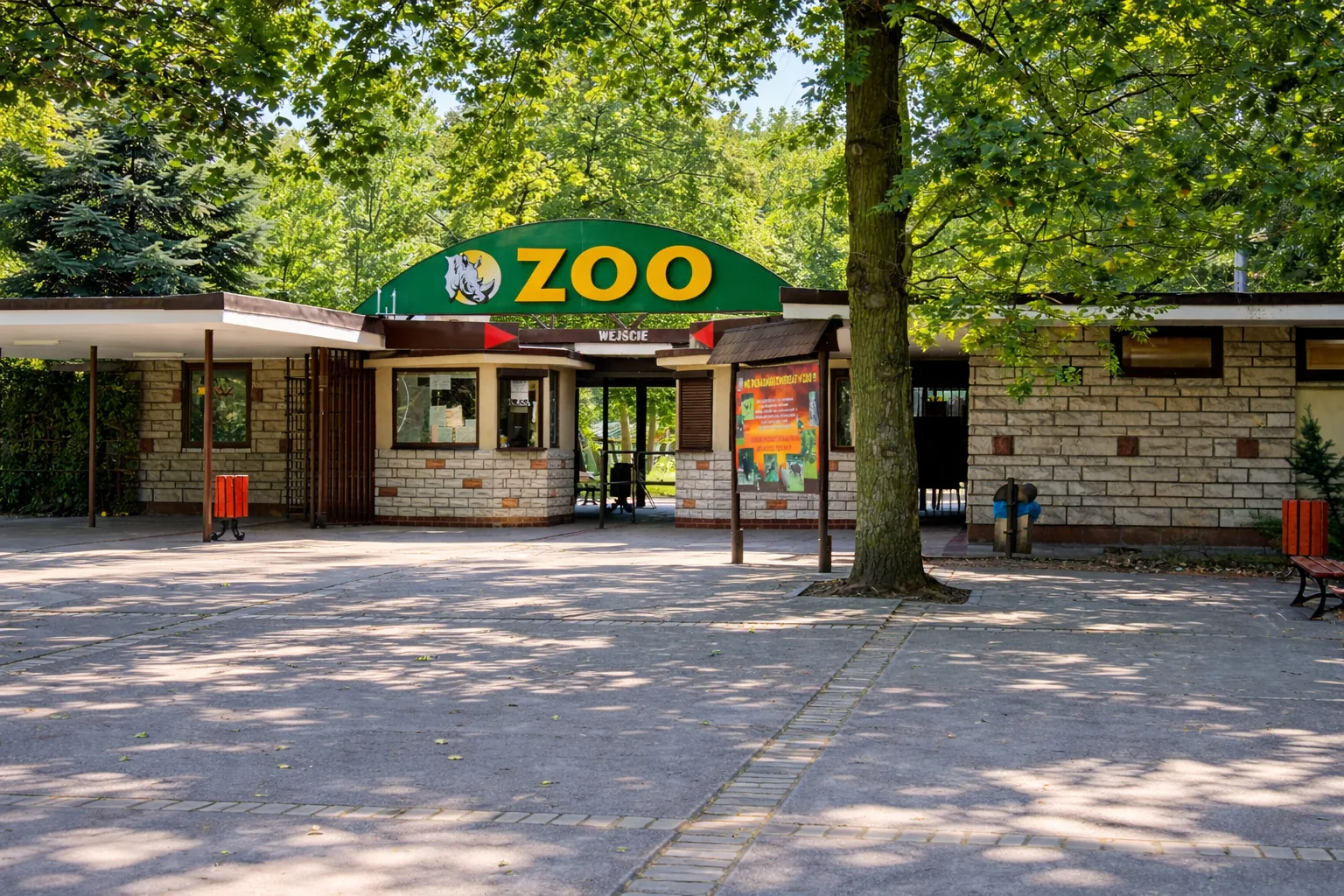 Wejście do Starego Zoo w Poznaniu z zielonym szyldem ZOO wśród drzew.