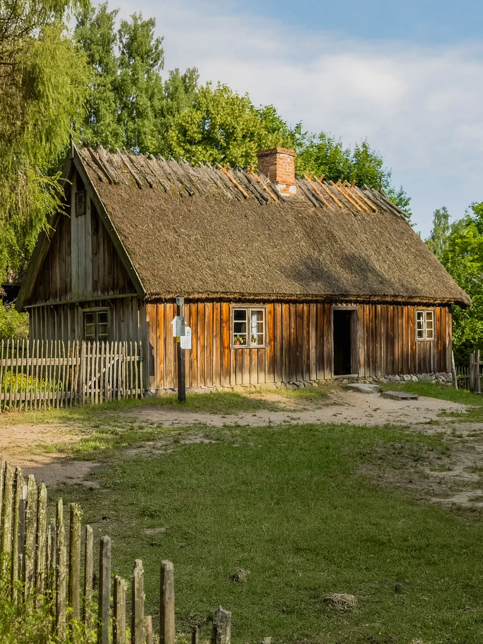 Drewniana chata kryta strzechą w Kaszubskim Parku Etnograficznym we Wdzydzach – tradycyjna wiejska zabudowa z drewnianym płotem