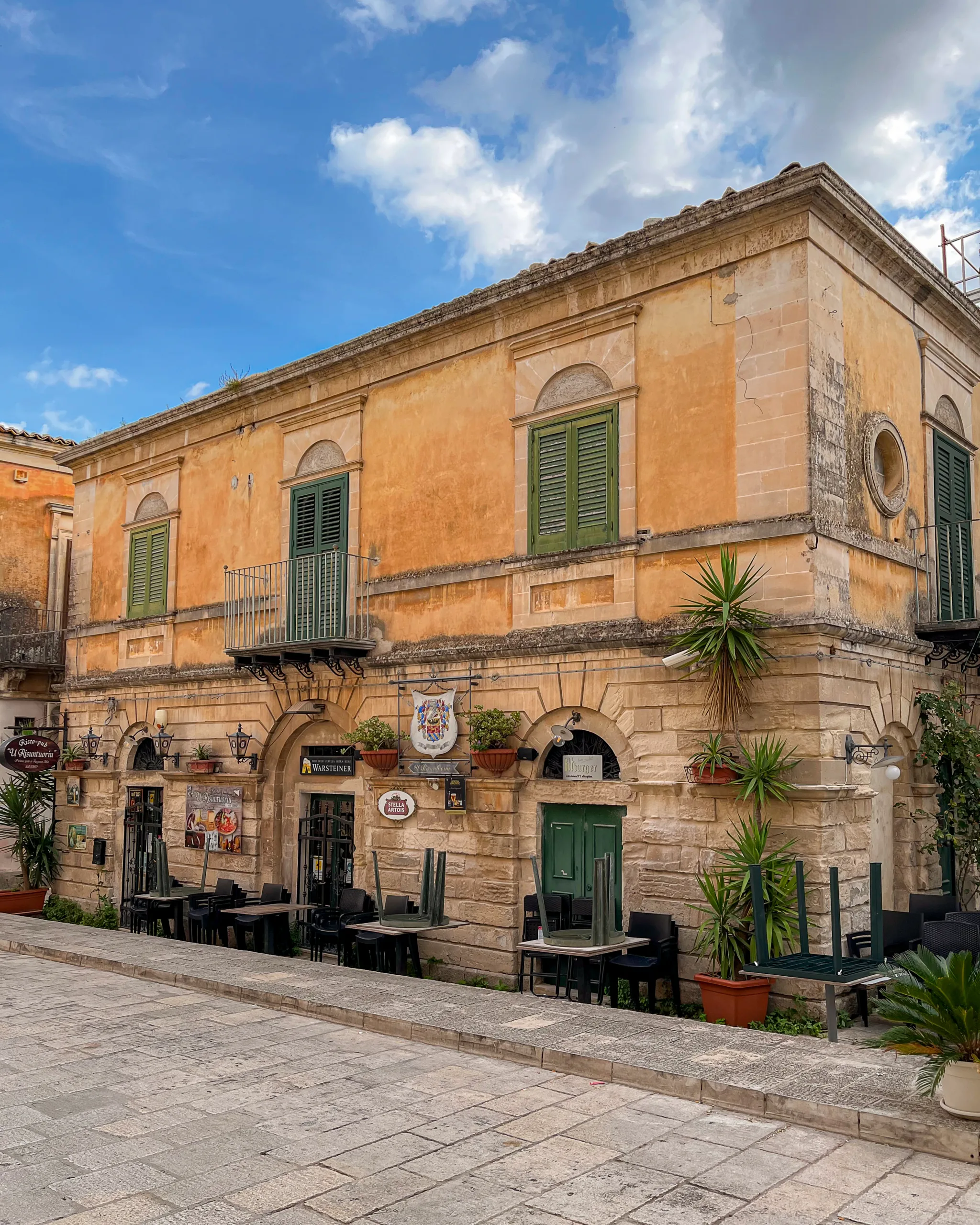 Zabytkowa kamienica z zielonymi okiennicami i restauracją w historycznym centrum Ragusa Ibla