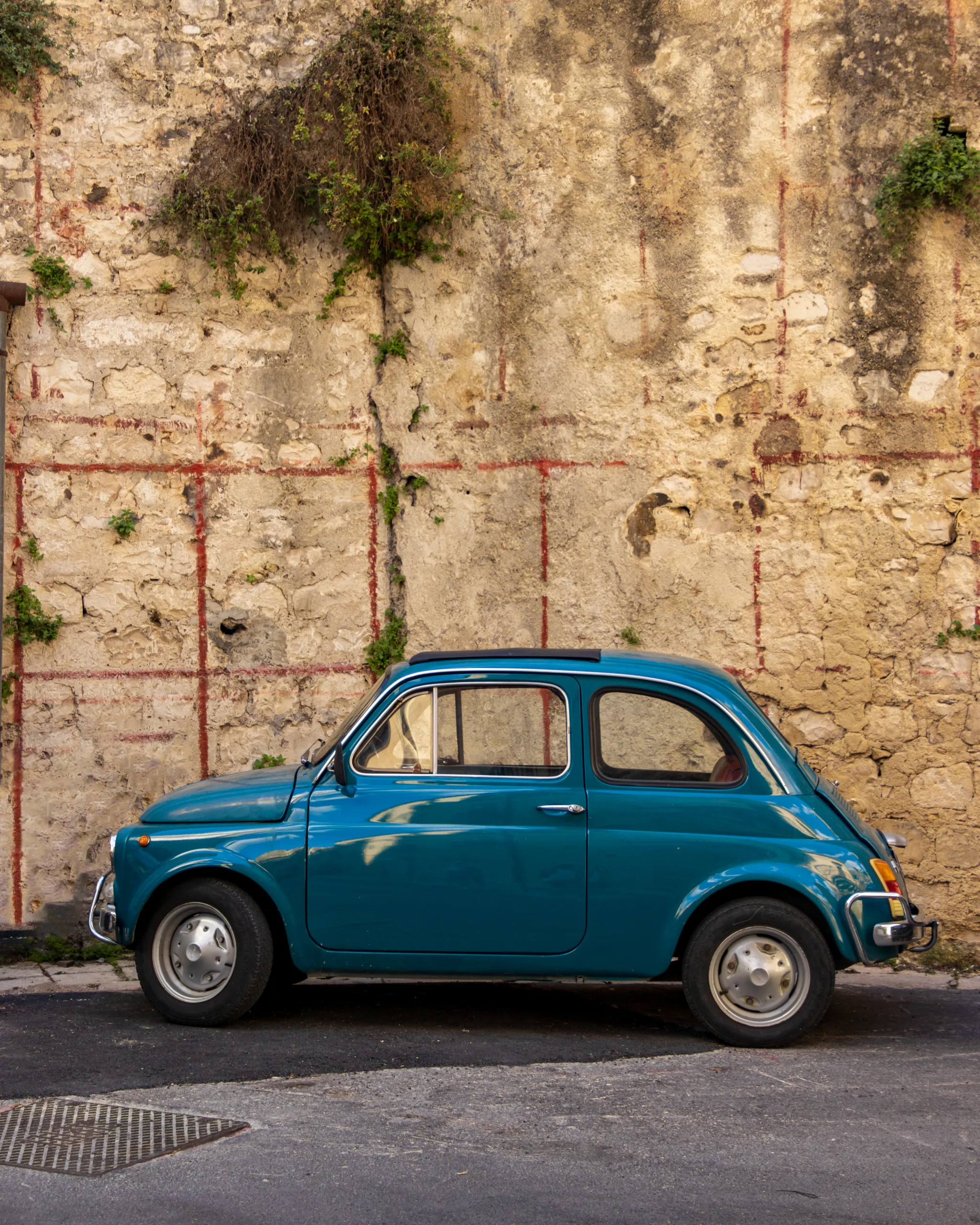 Niebieski Fiat 500 zaparkowany przy starej kamiennej ścianie w Modice na Sycylii