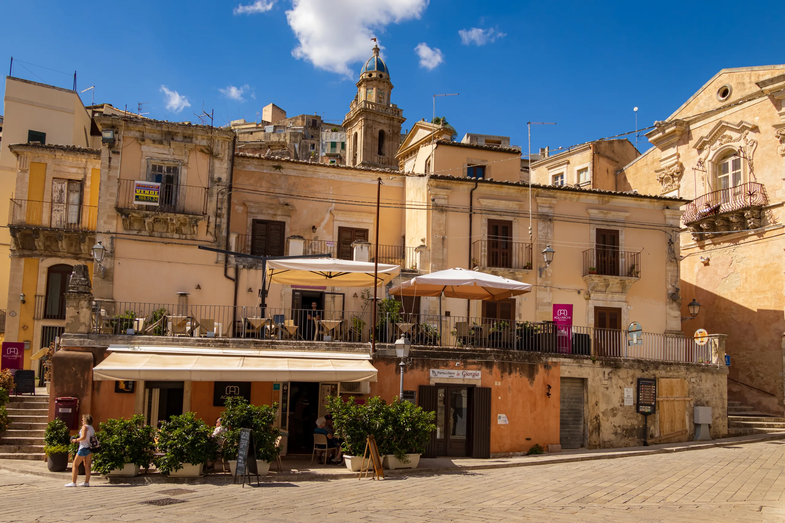 Ragusa na Sycylii z zabytkowymi kamienicami, tarasami restauracji i wieżą kościoła w historycznym centrum miasta