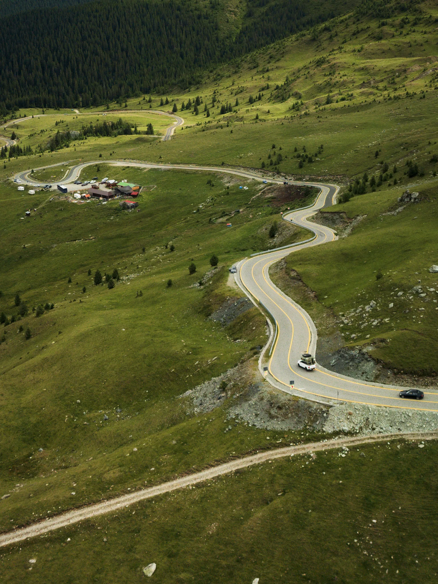 Kręta Trasa Transalpina wijąca się przez zielone górskie zbocza i polany w Rumunii.