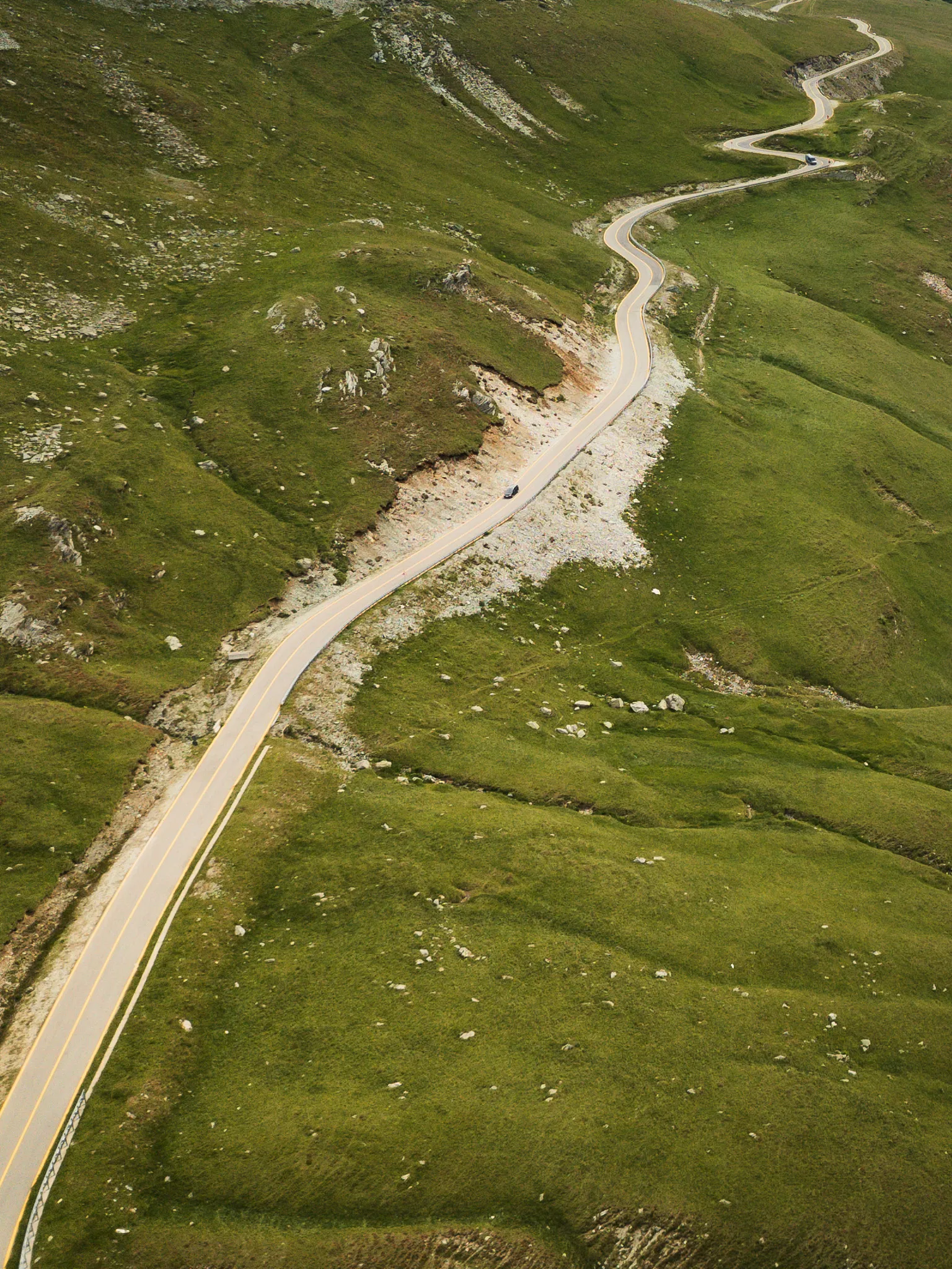Kręta Trasa Transalpina prowadząca przez rozległe zielone zbocza gór Parâng w Rumunii.