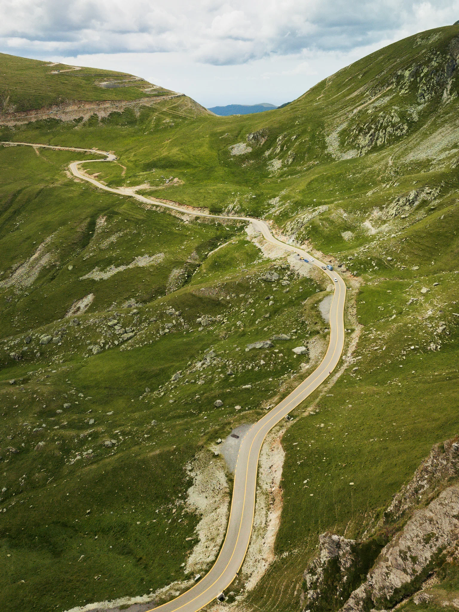 Widok z drona na Trasę Transalpina wijącą się przez wysokogórskie zbocza pod pochmurnym niebem.