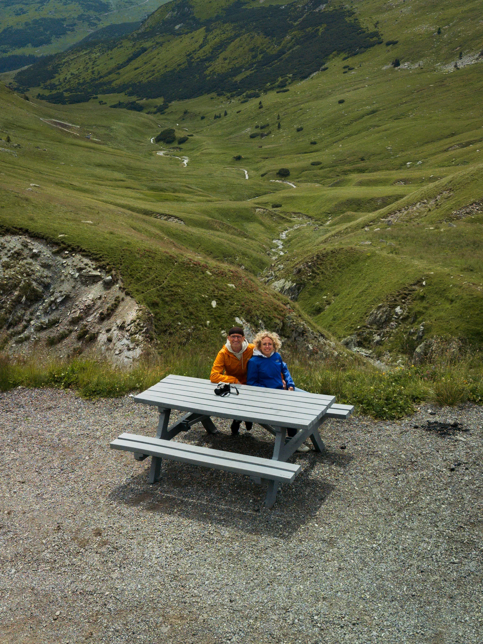 Para stojąca przy ławie piknikowej na tle rozległej doliny w górach Parâng przy Trasie Transalpina.