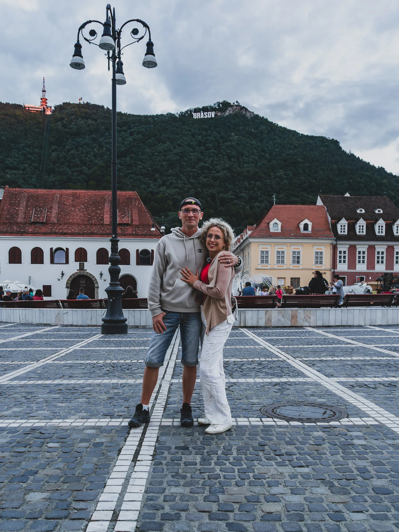 Para na placu Piața Sfatului w Braszowie, ze wzgórzem Tâmpa i napisem BRASOV w tle.