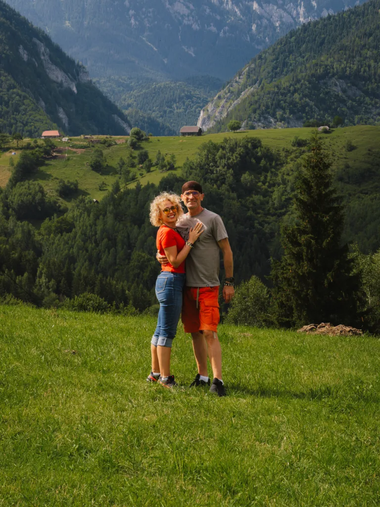 Para na zielonej łące w wiosce Măgura w Rumunii, z górską doliną i zalesionymi zboczami Karpat w tle.