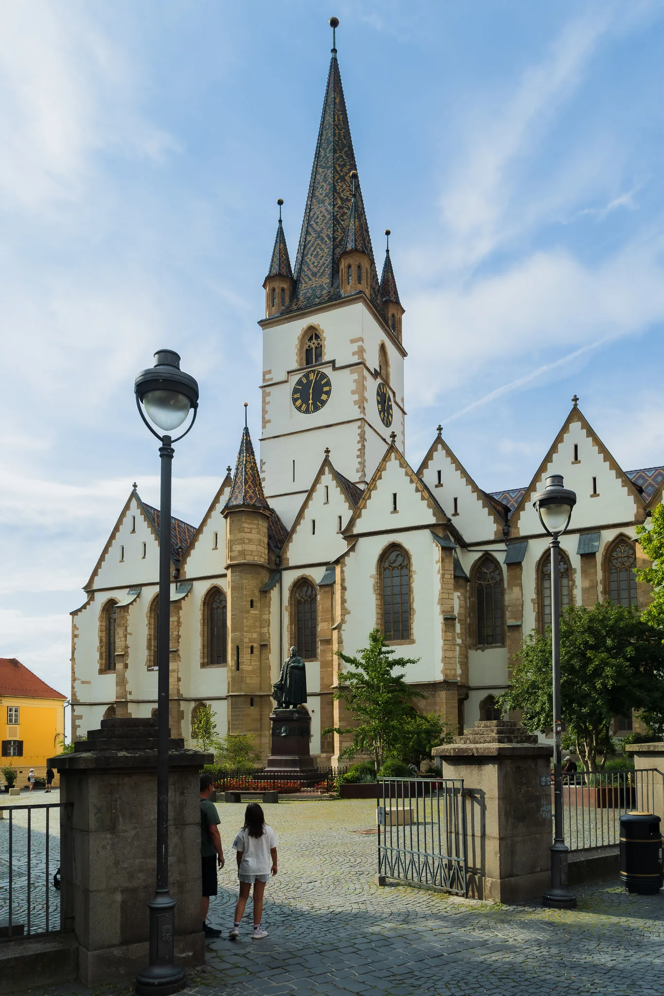 Katedra ewangelicka w Sybinie widziana od strony placu, z wysoką wieżą zegarową, ozdobnym dachem i brukowanym dziedzińcem na pierwszym planie.