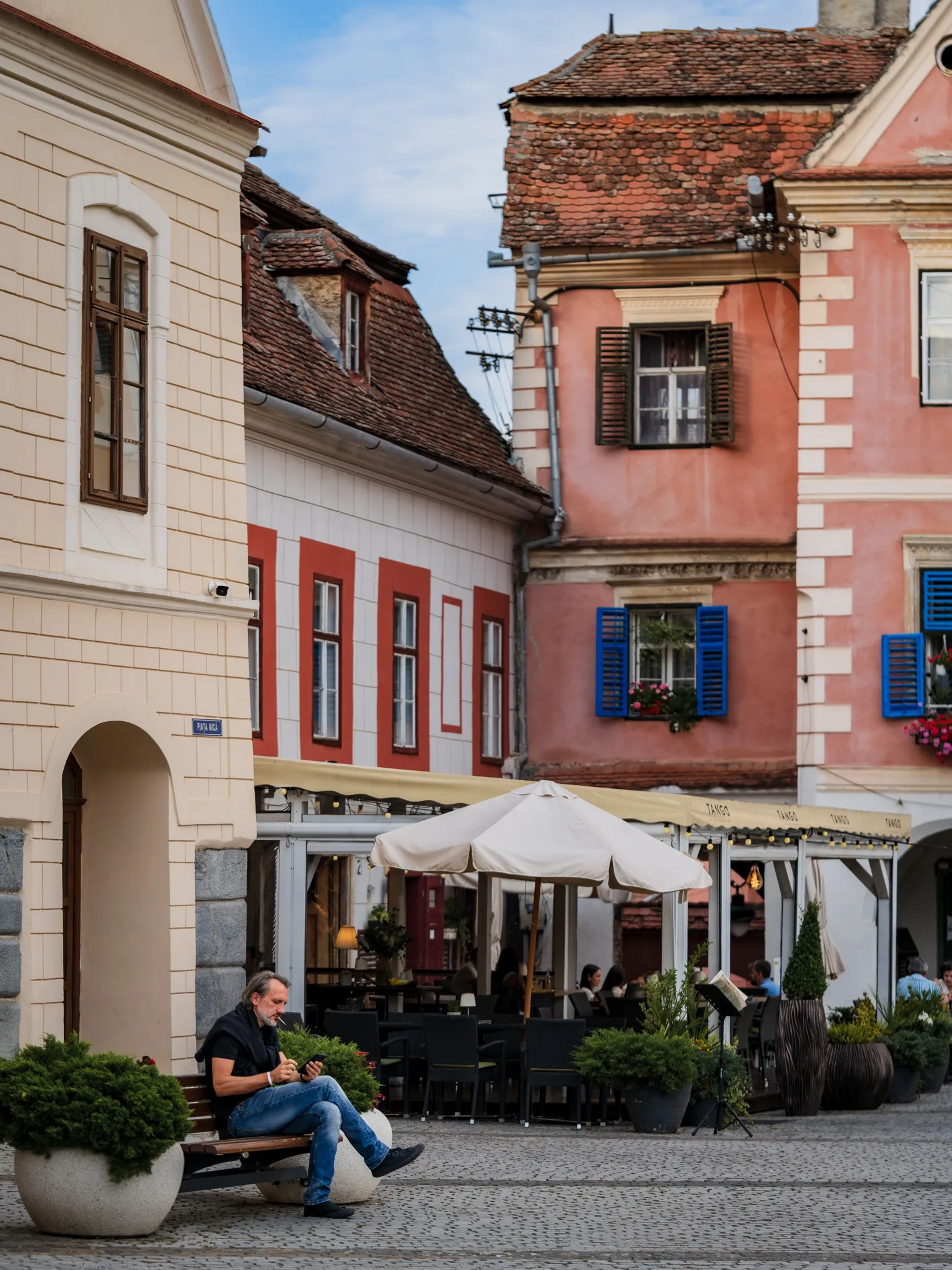 Kolorowe kamienice przy Małym Rynku w Sybinie, restauracyjne ogródki i mężczyzna siedzący na ławce.