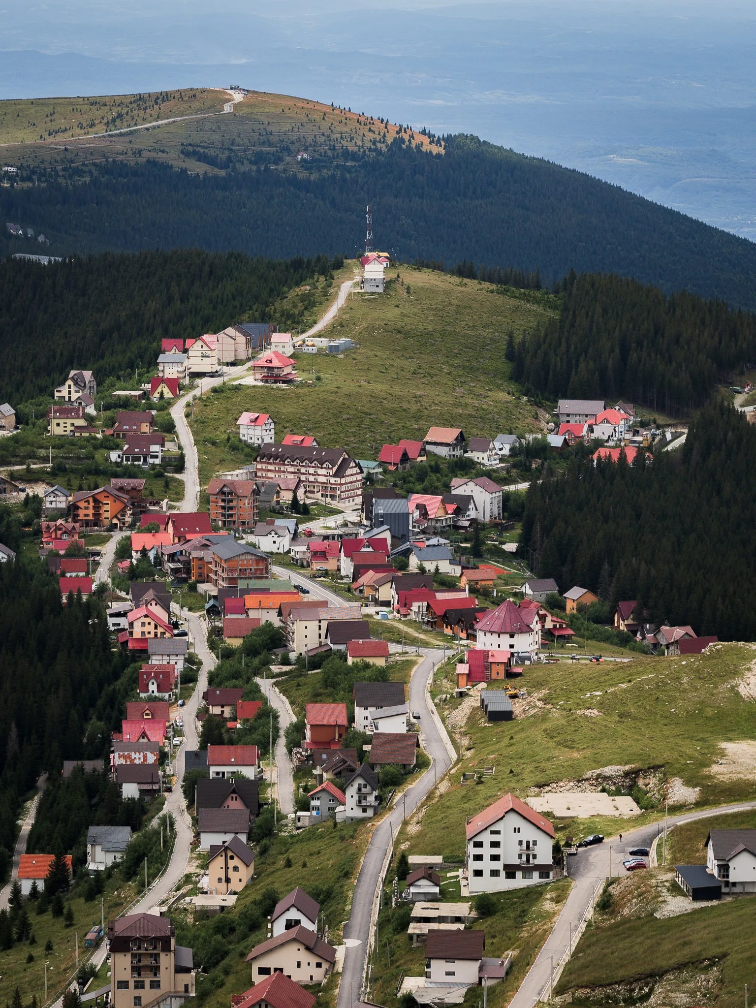 Widok z góry na górską miejscowość Rânca położoną przy Trasie Transalpina, w otoczeniu lasów i zboczy.