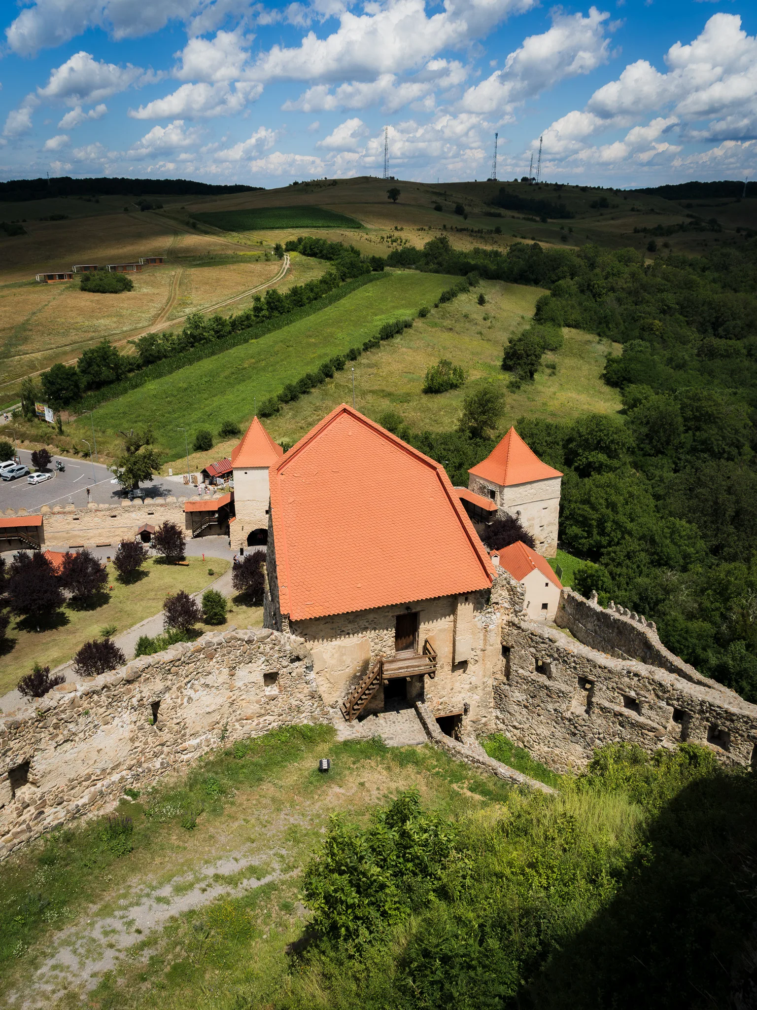 Dziedziniec twierdzy Rupea z kamiennymi murami, budynkiem z czerwonym dachem i zielonymi wzgórzami w tle