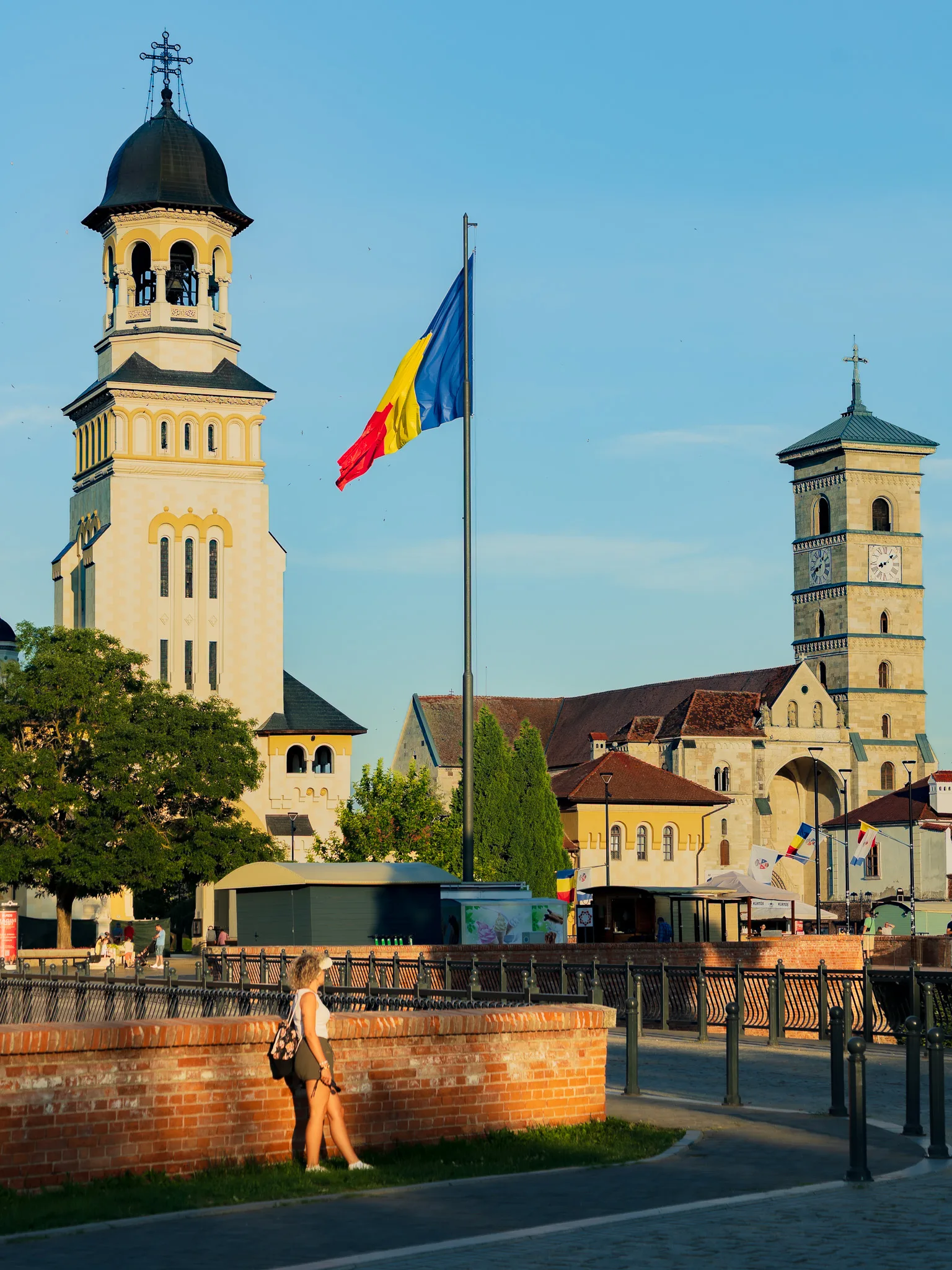 Katedra Koronacyjna i katedra św. Michała w Alba Iulia z flagą Rumunii oraz spacerującą kobietą na pierwszym planie.