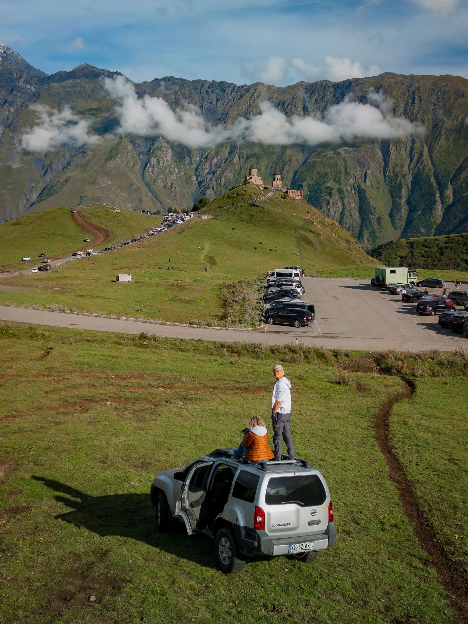 Nissan Xterra 4x4 i para podróżników z widokiem na cerkiew Cminda Sameba w Gergeti koło Stepancmindy. Gruzja samochodem.