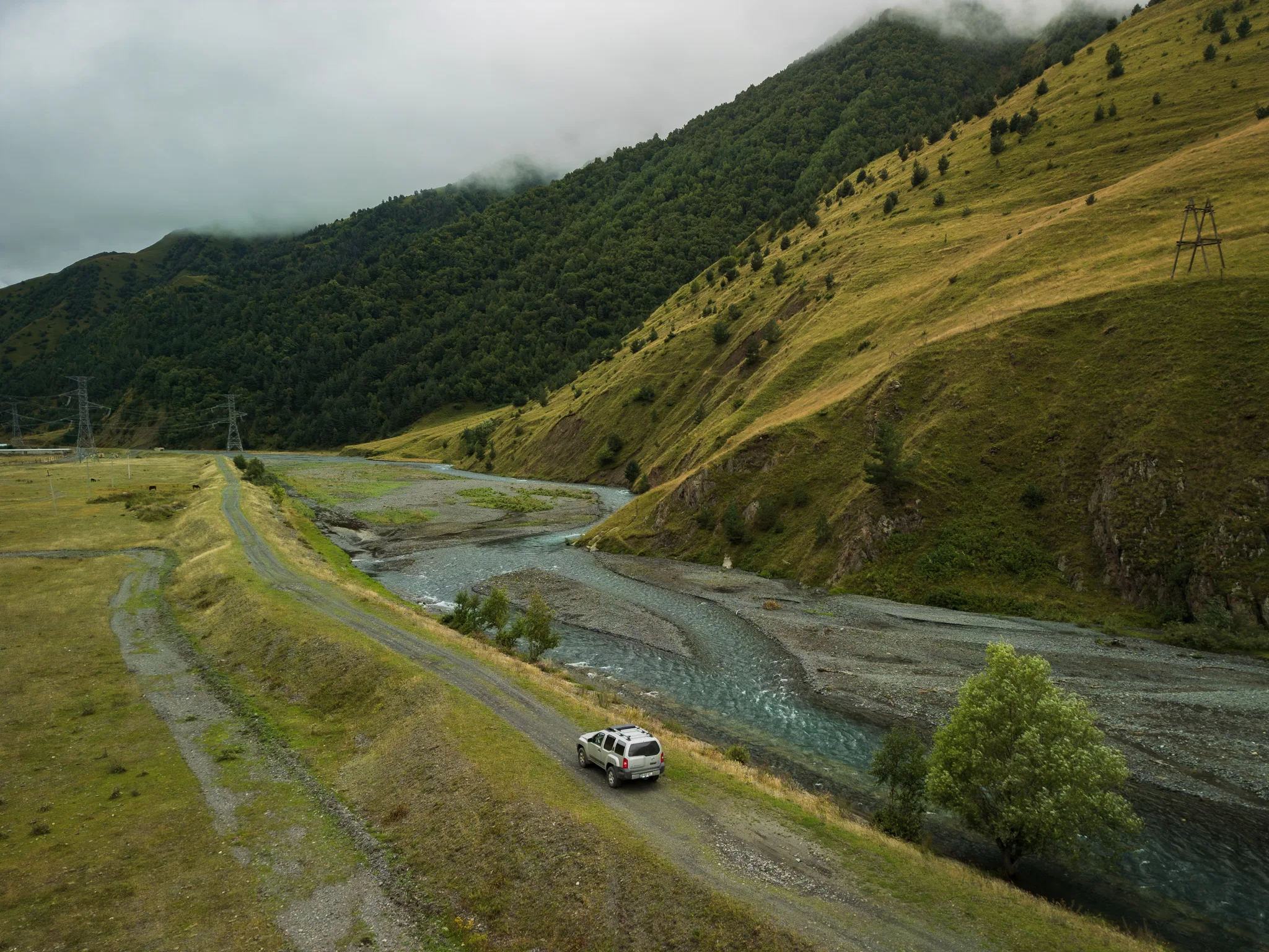 Nissan Xterra 4x4 na szutrowej drodze prowadzącej do Juty w Gruzji, wzdłuż górskiej rzeki i zielonych zboczy Kaukazu.