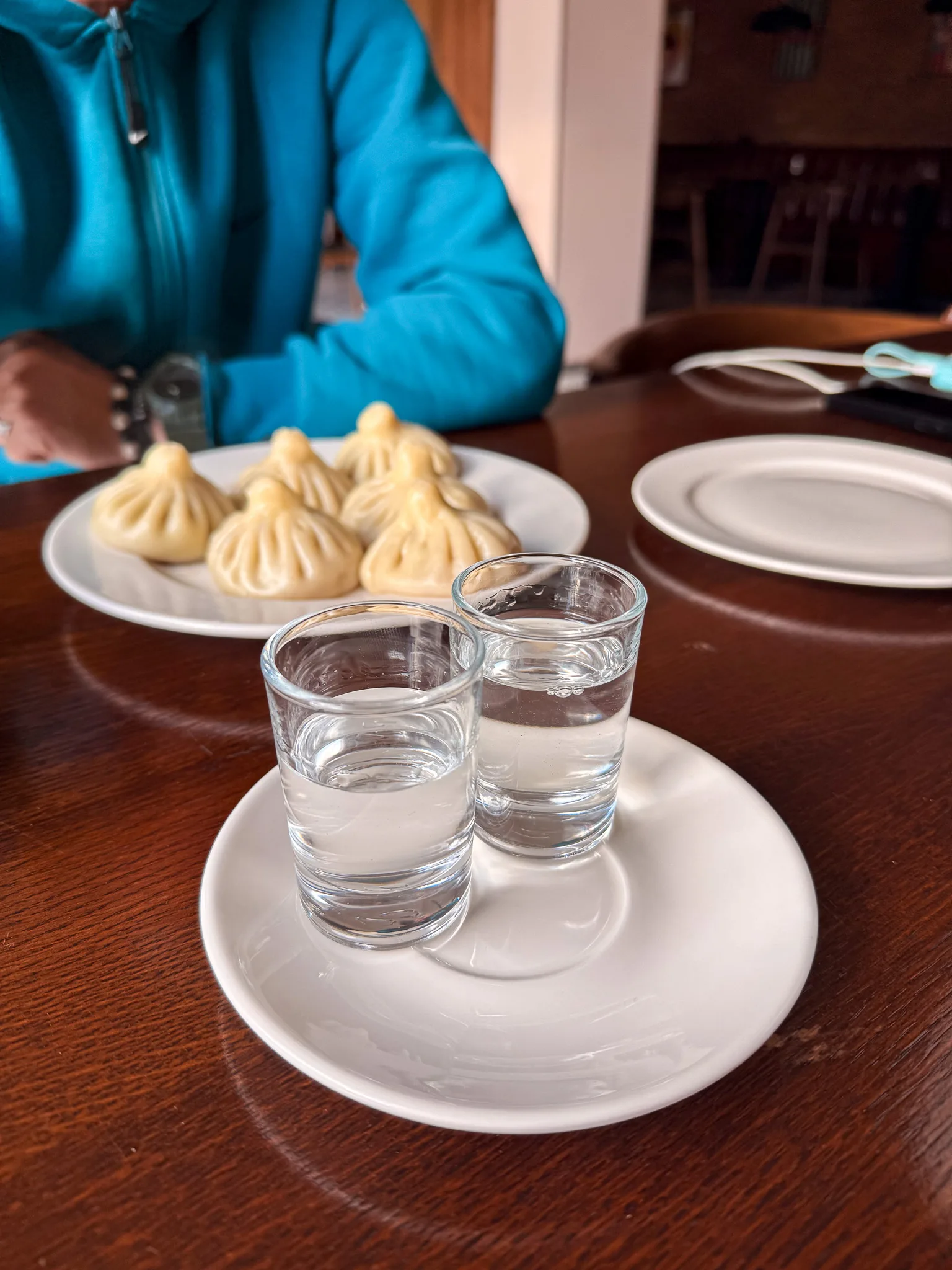 Gruzińska czacza w dwóch kieliszkach na białym talerzyku, a w tle tradycyjne pierożki chinkali podane w restauracji w Gruzji.