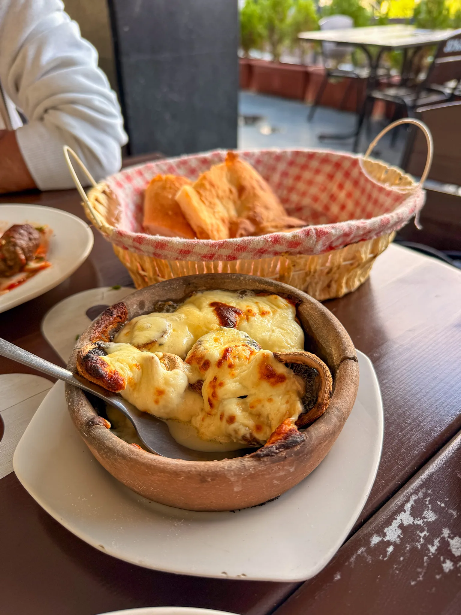 Pieczarki zapiekane pod roztopionym serem w glinianym naczyniu, podane z gruzińskim pieczywem w restauracji.