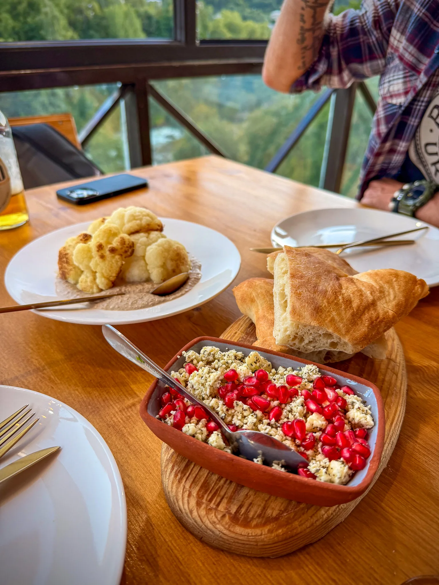 Gruzińskie przystawki – sałatka z ziarnami granatu i orzechami, pieczony kalafior w sosie oraz świeże pieczywo na stole w restauracji.
